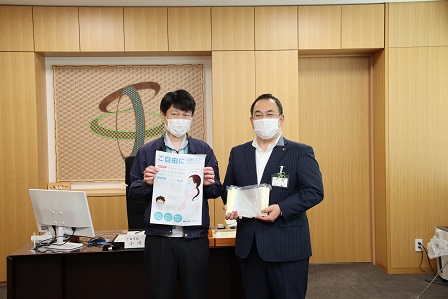 チラシを手に持った職員の男性がマスクをしながらカメラのほうを向いている写真