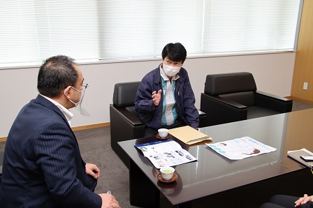 フェイスシールドをした市長とマスクをしている工場長が椅子に座って対面している写真
