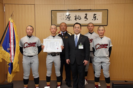 ユニフォームを着た千曲ボーイズと市長が壁際に並んで立って記念撮影をしている写真