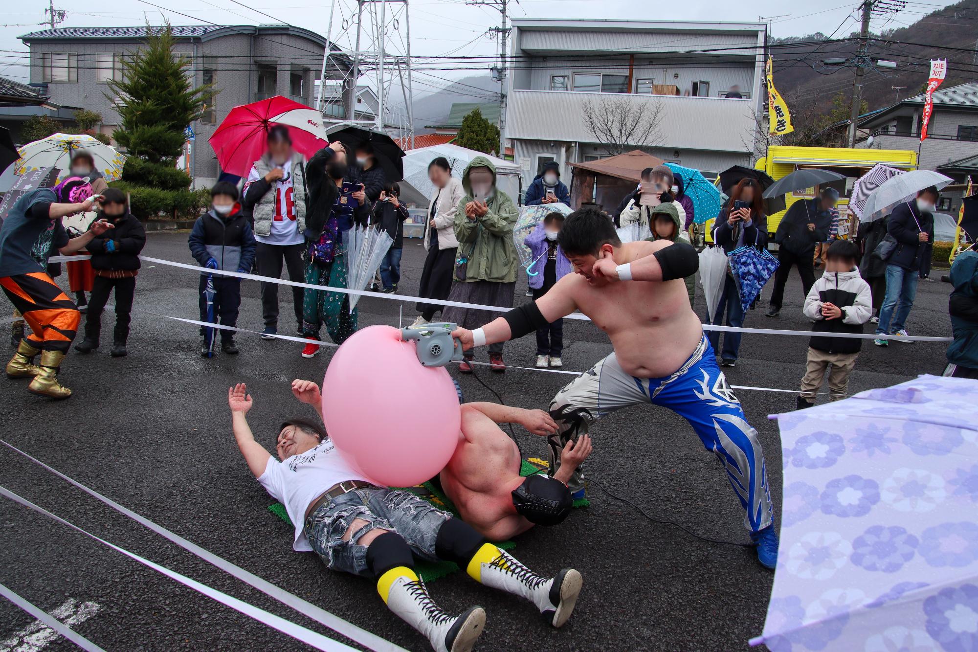信州プロレスの試合で、巨大風船を使って相手選手を倒している様子