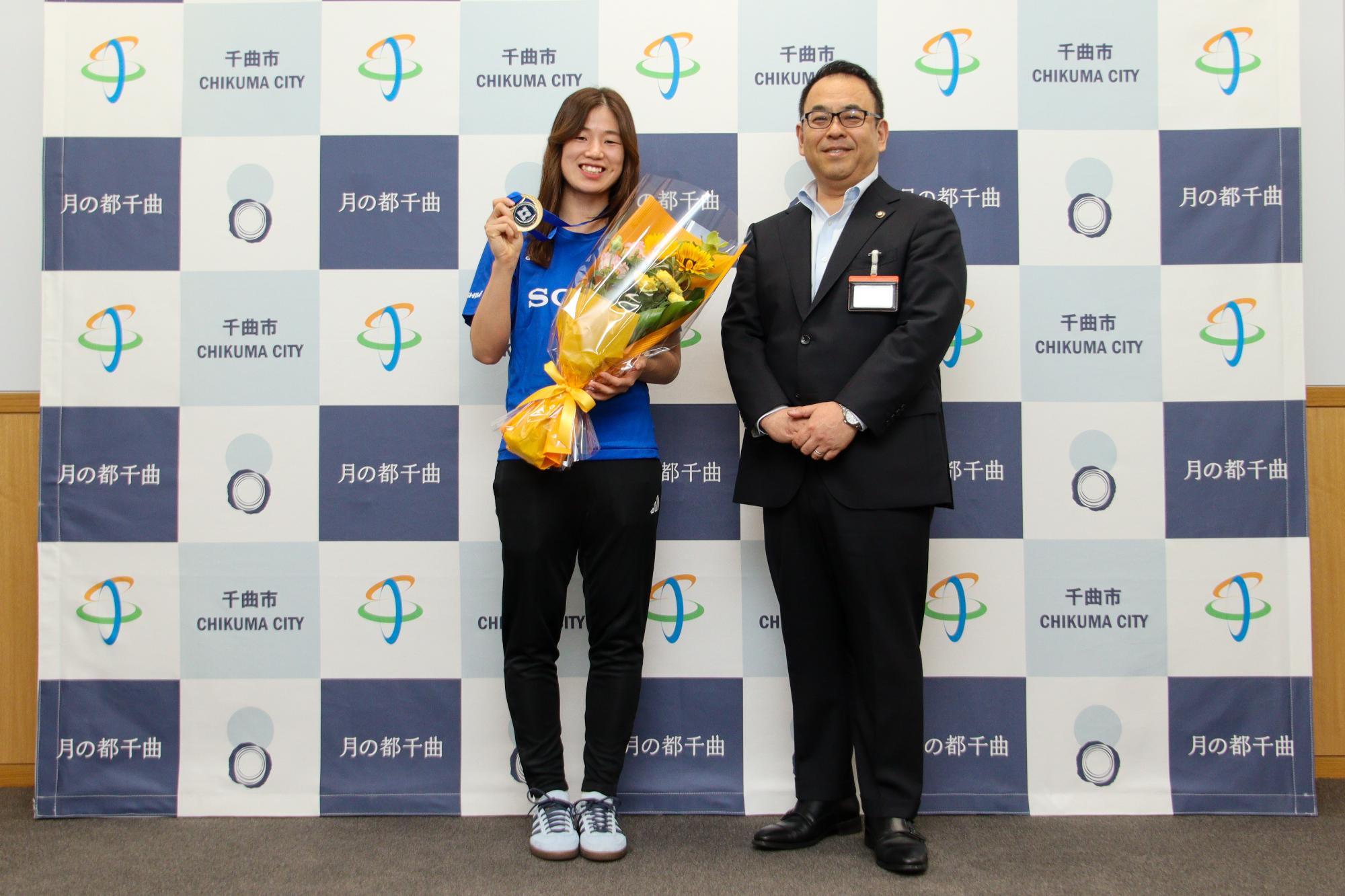花束とメダルを掲げる笠井選手(左)と小川市長(右)