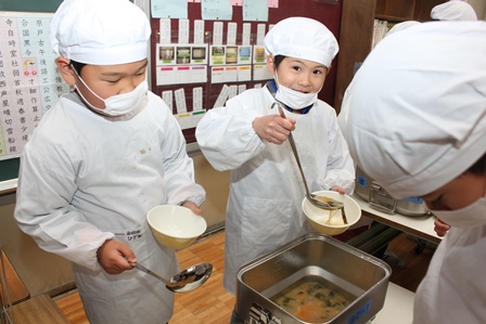 白衣、マスク、給食帽を身につけ、スープを器によそう児童達の写真