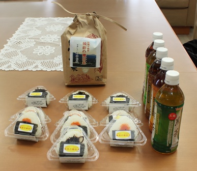 机にお米のパッケージ、おにぎり、お茶が並んだ写真