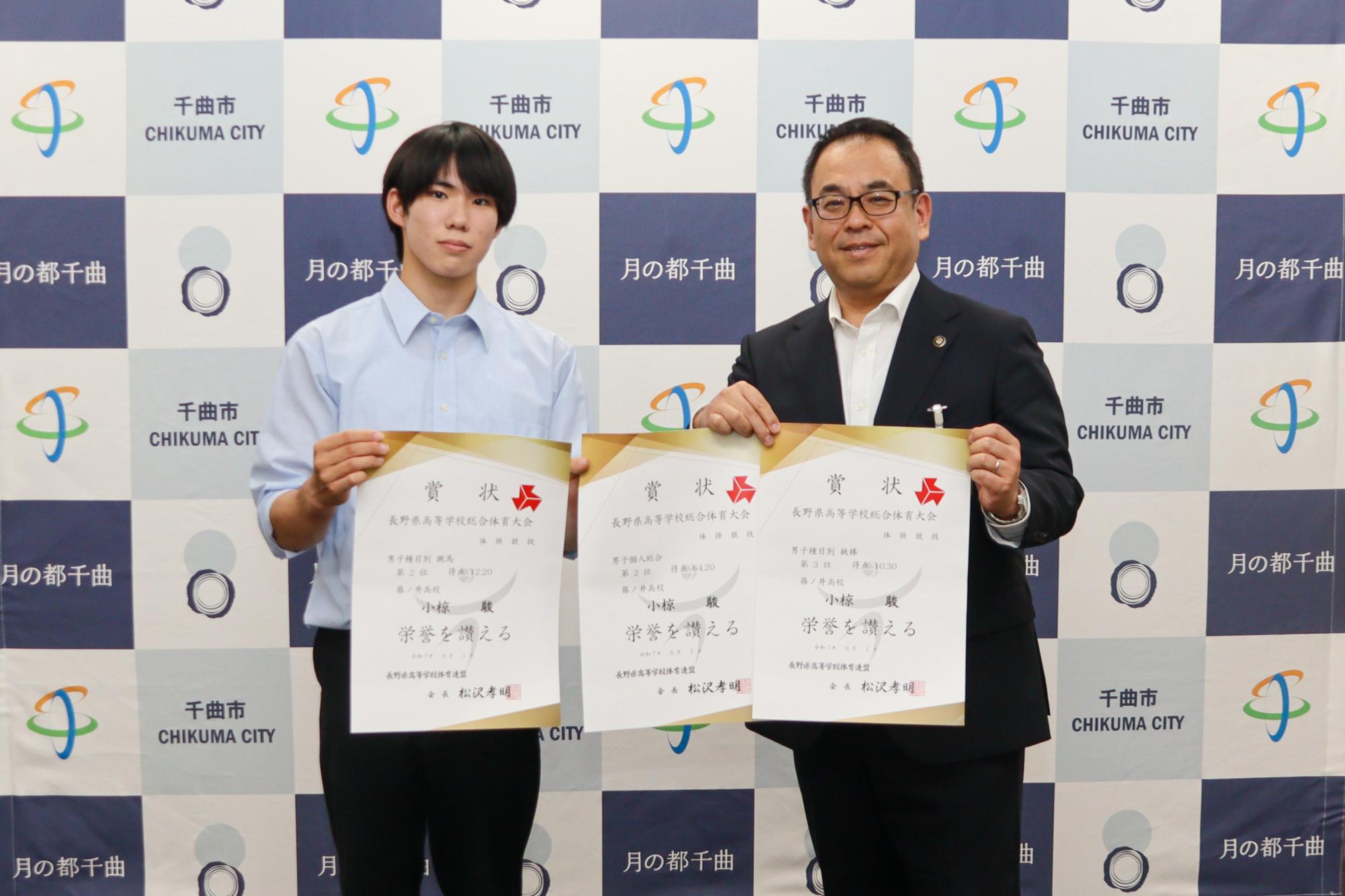 個人総合の賞状1枚と種目別の賞状2枚の合計3枚の賞状を持って記念撮影する小椋さん(左)と小川市長(右)