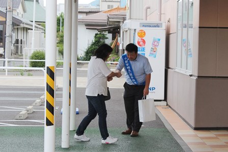 首からタスキをかけた男性がスーパーの前でチラシ入りティッシュを配布している写真