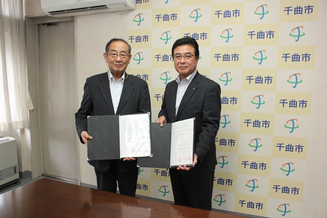 協定書を手にカメラのほうを向いて記念撮影をする市長らの写真