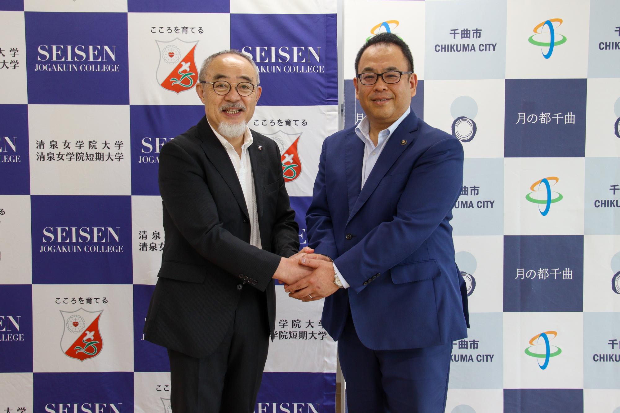 共同記者発表清泉女学院大学田村学長(左)と小川市長(右)が握手を交わしている様子
