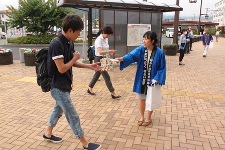 青色の半被を着た女性が駅前でティッシュを配っている写真