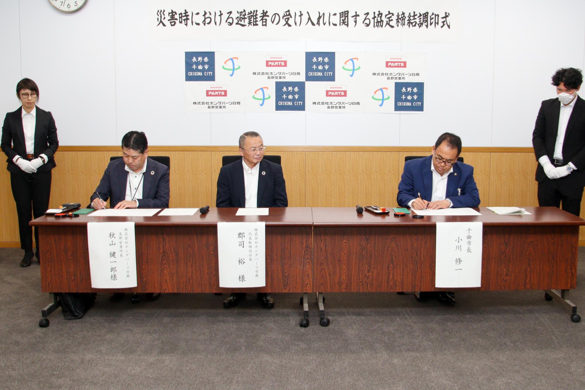 調印式で協定書の署名をする秋山長野営業所長(左)と小川市長(右)とそれを見守る郡司代表取締役社長(中央)