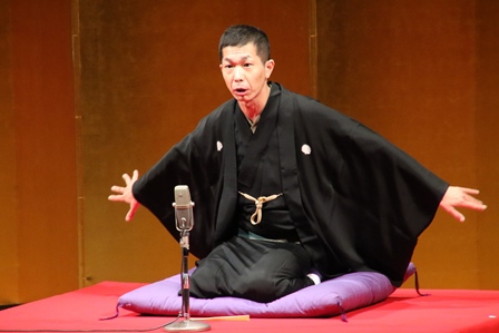 寄席で手をひろげて落語を話す林家三三さんの写真