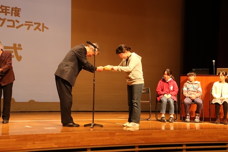 ホールのステージ上で表彰を受け取る小学生の女の子の写真