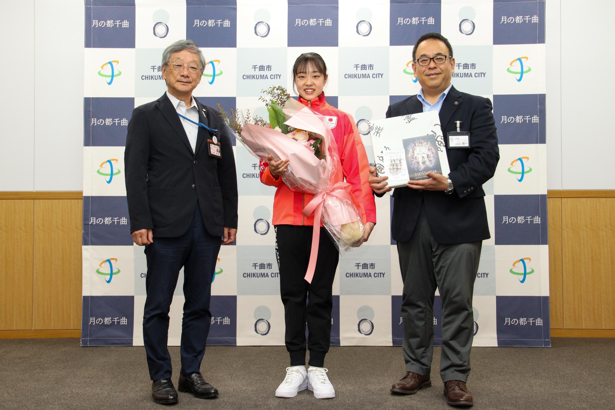 花束を手に記念撮影する和田選手(中央)と小川市長(右)、小松教育長(左)