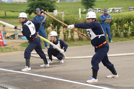 ホースや道具を持ち、姿勢を正して消火訓練を行う団員らの写真