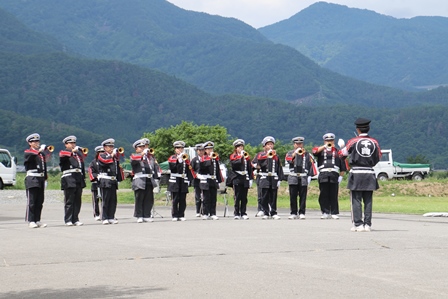 雄大な山を背景にラッパ分団の皆さんが整列している写真