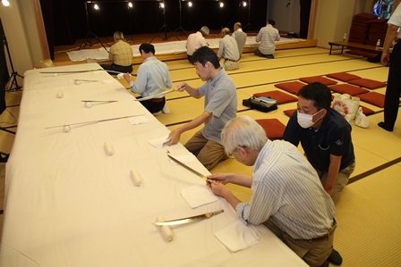 白いクロスの敷かれたテーブルの上にいくつもの刀が並んでいる写真