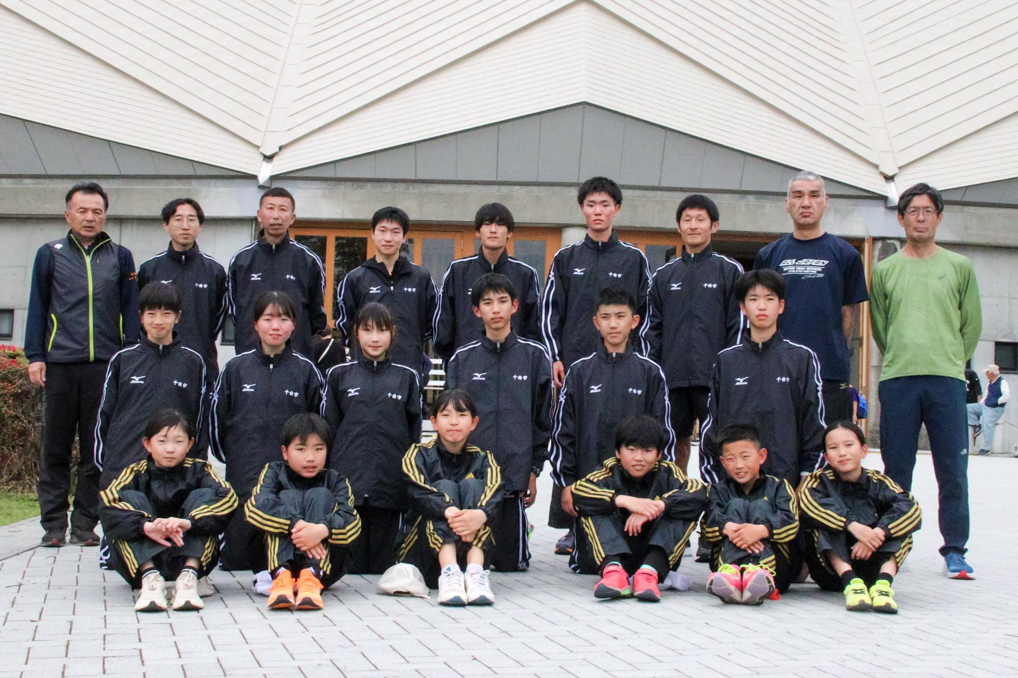 大会会場前での千曲市チーム集合写真、1列目小学生の部選手6名、2列目一般の部選手中学生6名、3列目一般の部選手高校生以上6名および監督コーチ3名