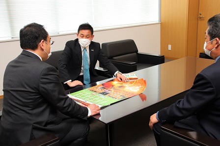 机にポスターを広げて話をしている市長と監督らの写真