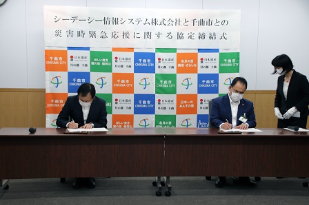 長机で書類に署名をしている市長と社長の写真
