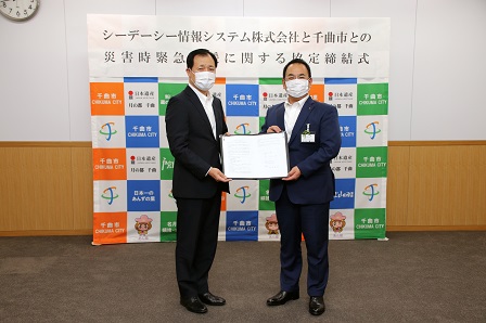 協定書をカメラに向かって見せながら立っている市長と社長の写真