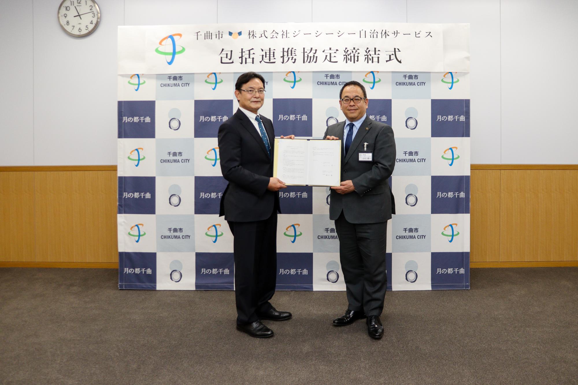 協定書を2人で持って記念撮影する岡田社長(左)と小川市長(右)