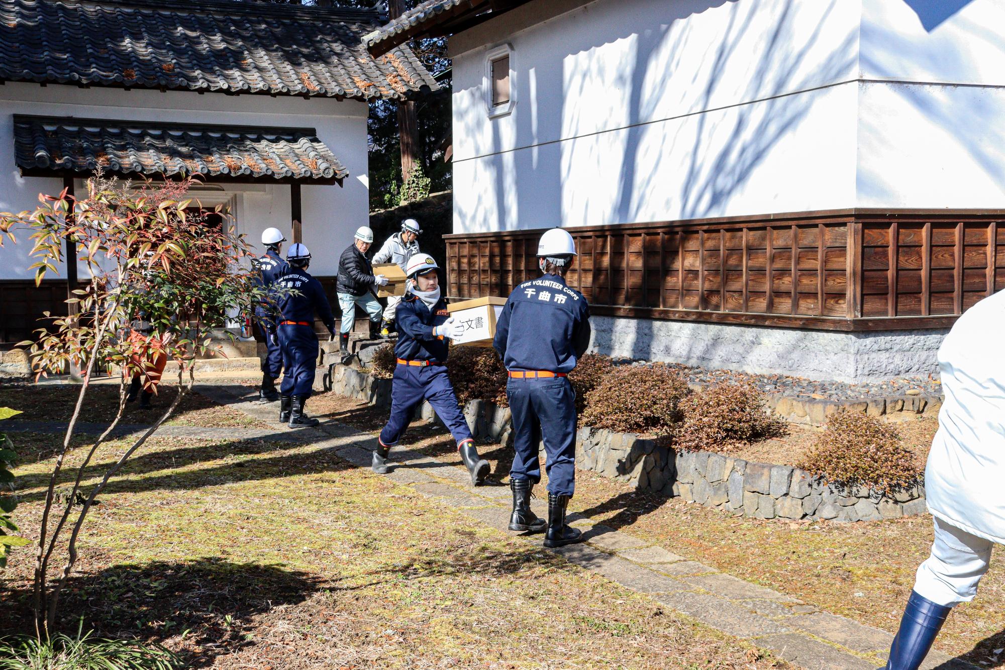 消防団員と市職員が縦に並び、収蔵庫から古文書に見立てた段ボールの文書保存箱を手渡しで搬出する訓練の様子