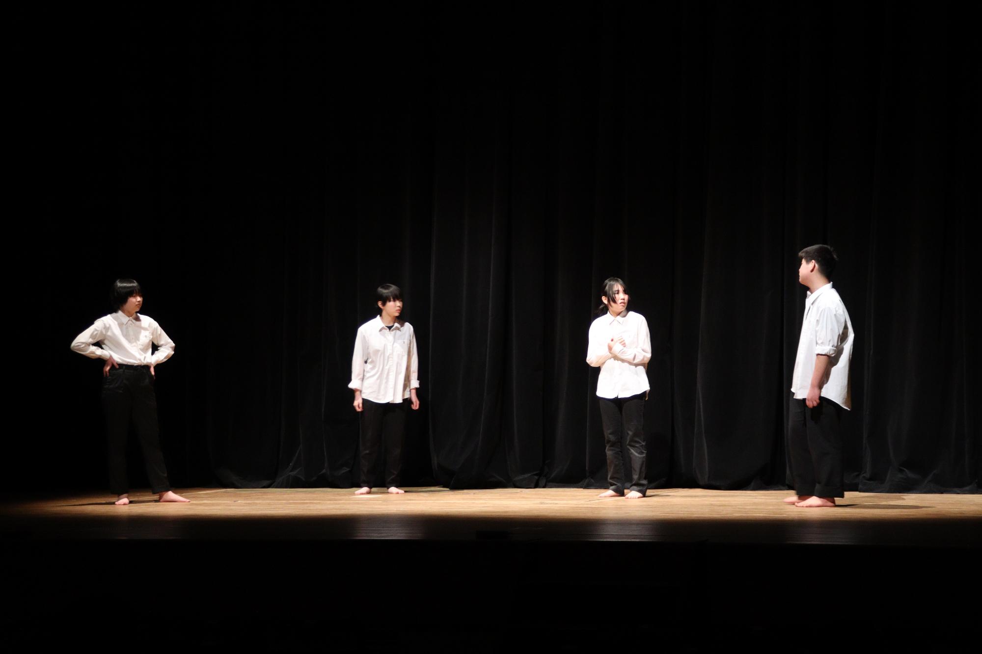 屋代高校と同附属中学校演劇班による「ある脱出ゲーム」のシーンの一部。4人の男女が閉じ込められた部屋から脱出しようと立ち上がった状態で話し合っている様子。