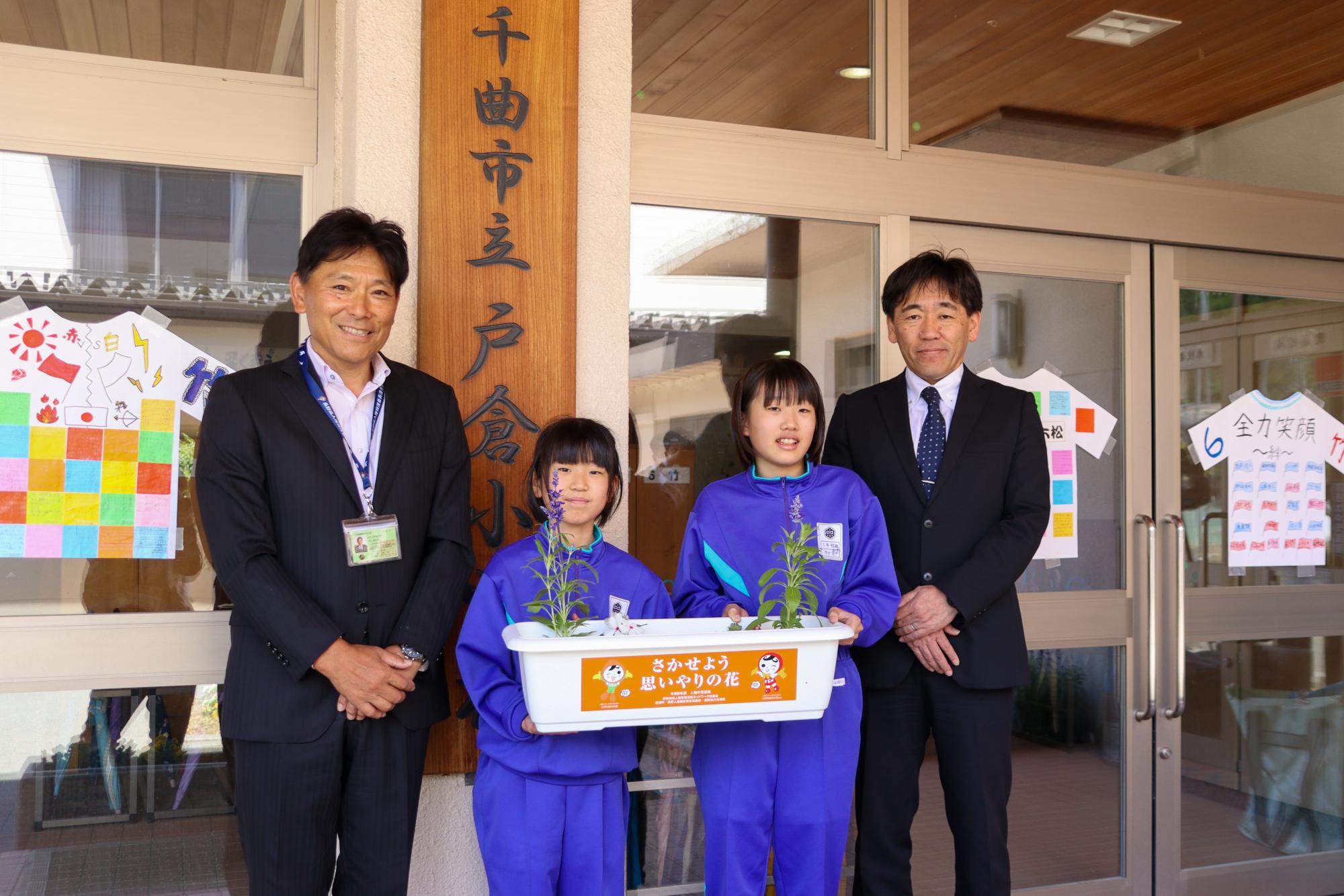 手渡されたプランターを持って記念撮影する4人(左から櫻井人権委員、小西さん、原田さん、尾臺校長)