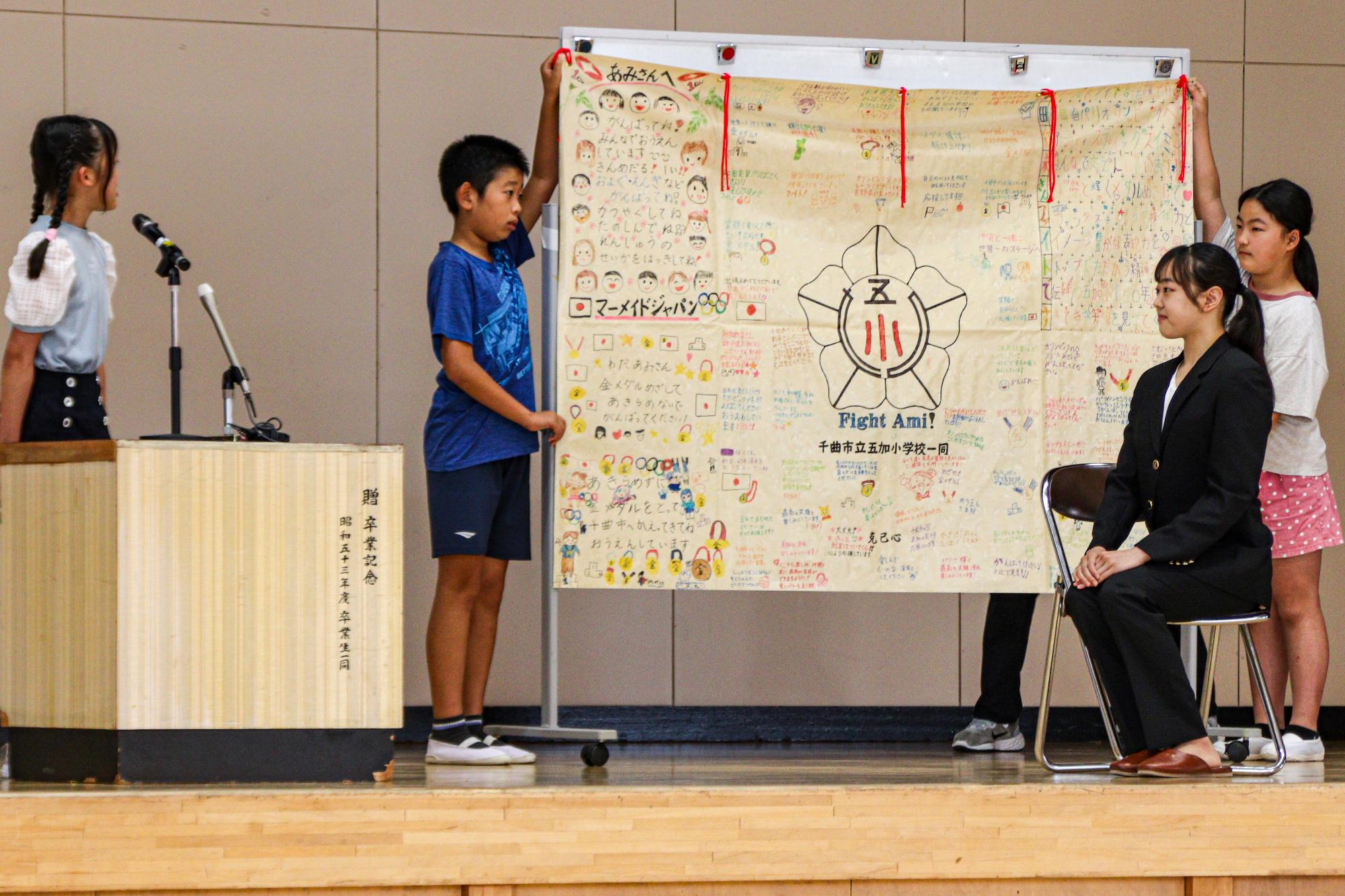 五加小学校体育館で応援メッセージの書かれた垂れ幕を紹介する児童とそれを聞く和田選手