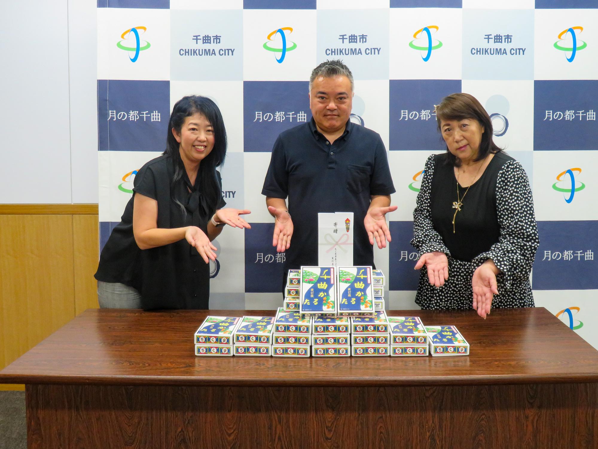 贈呈した千曲かるたを前に、ちくま未来フェスタ実行委員会の3人が記念撮影