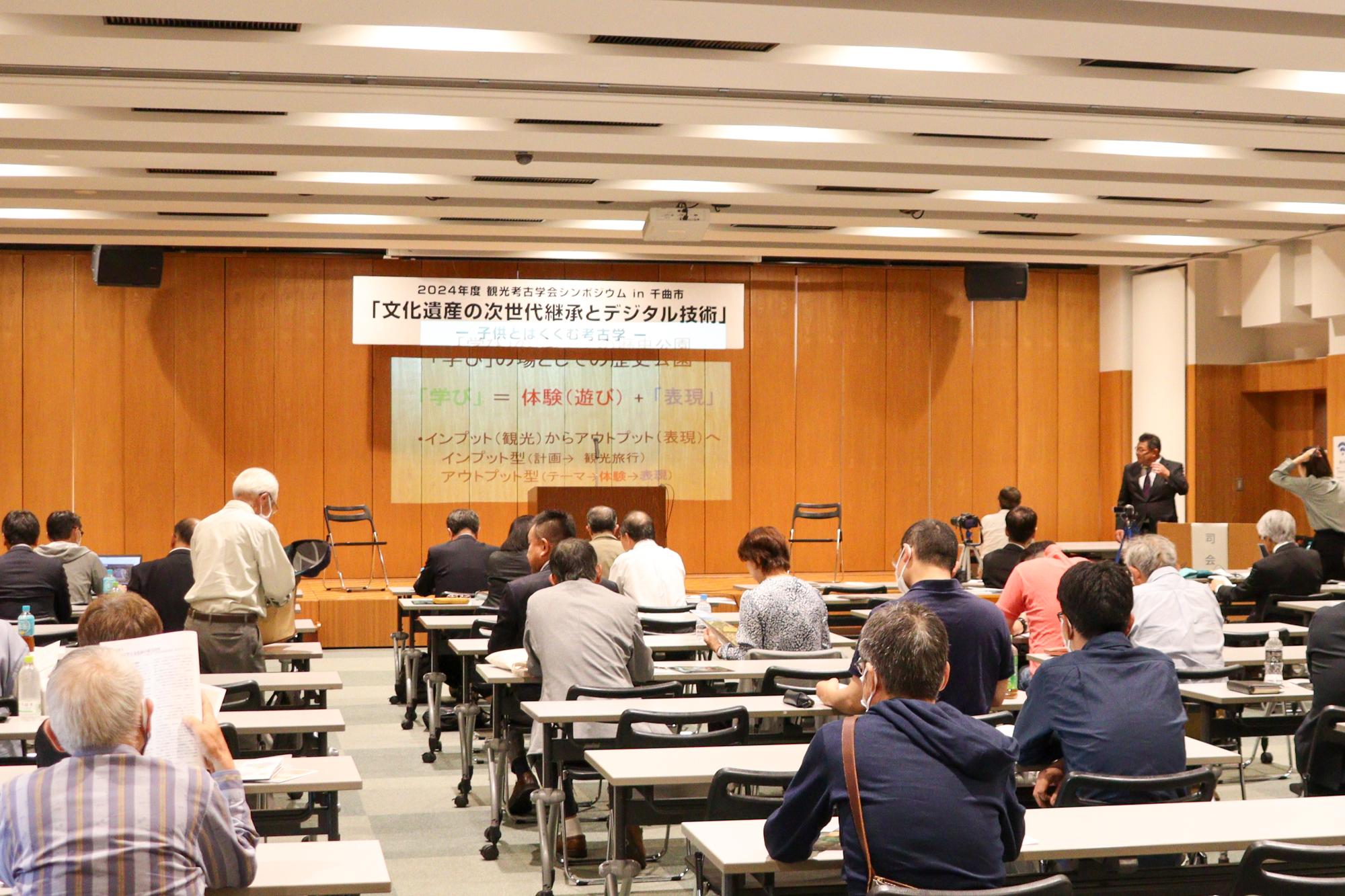 シンポジウムの会場の様子を後方から撮影_参加者23人程度が着席し前方を向いている