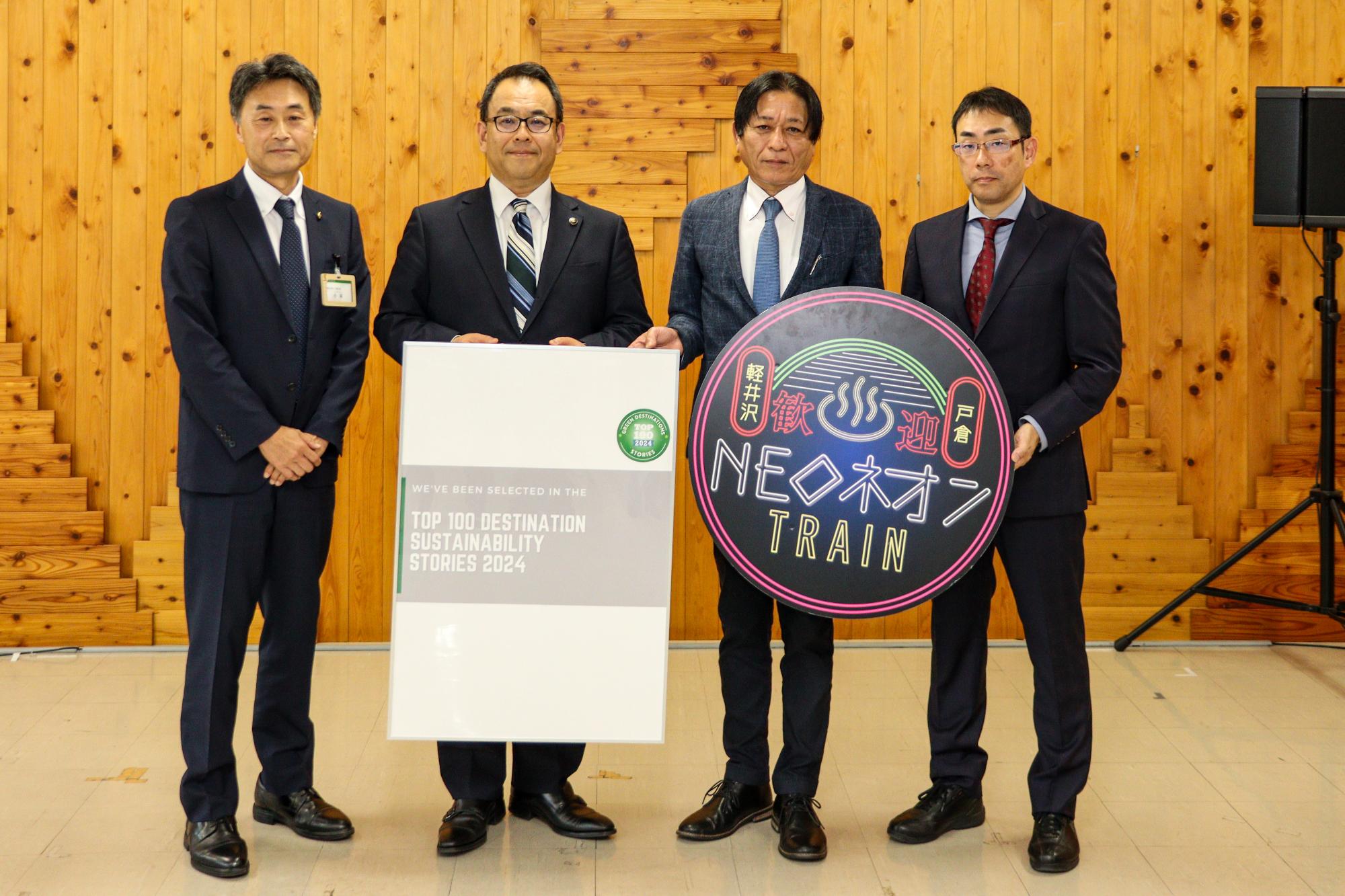 受賞のポスターとNEOネオンの看板を持って記念撮影する4人。左から長野県小林信之観光スポーツ部次長、千曲市小川修一市長、一般社団法人信州千曲観光局小沼浩栄専務理事、一般社団法人長野県観光機構中島邦雄常務理事