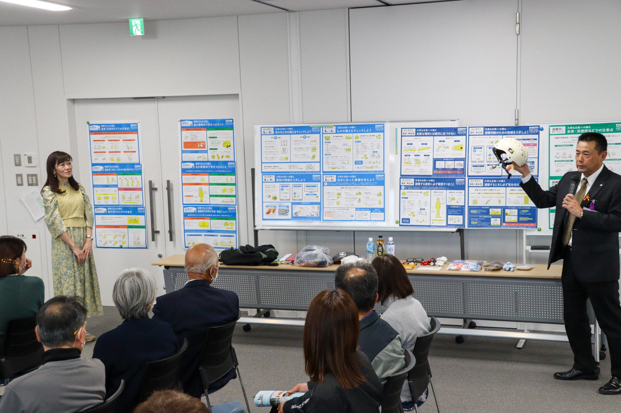 防災用品の展示について解説する横林危機管理担当担当部長とそれを聞く鈴木さん