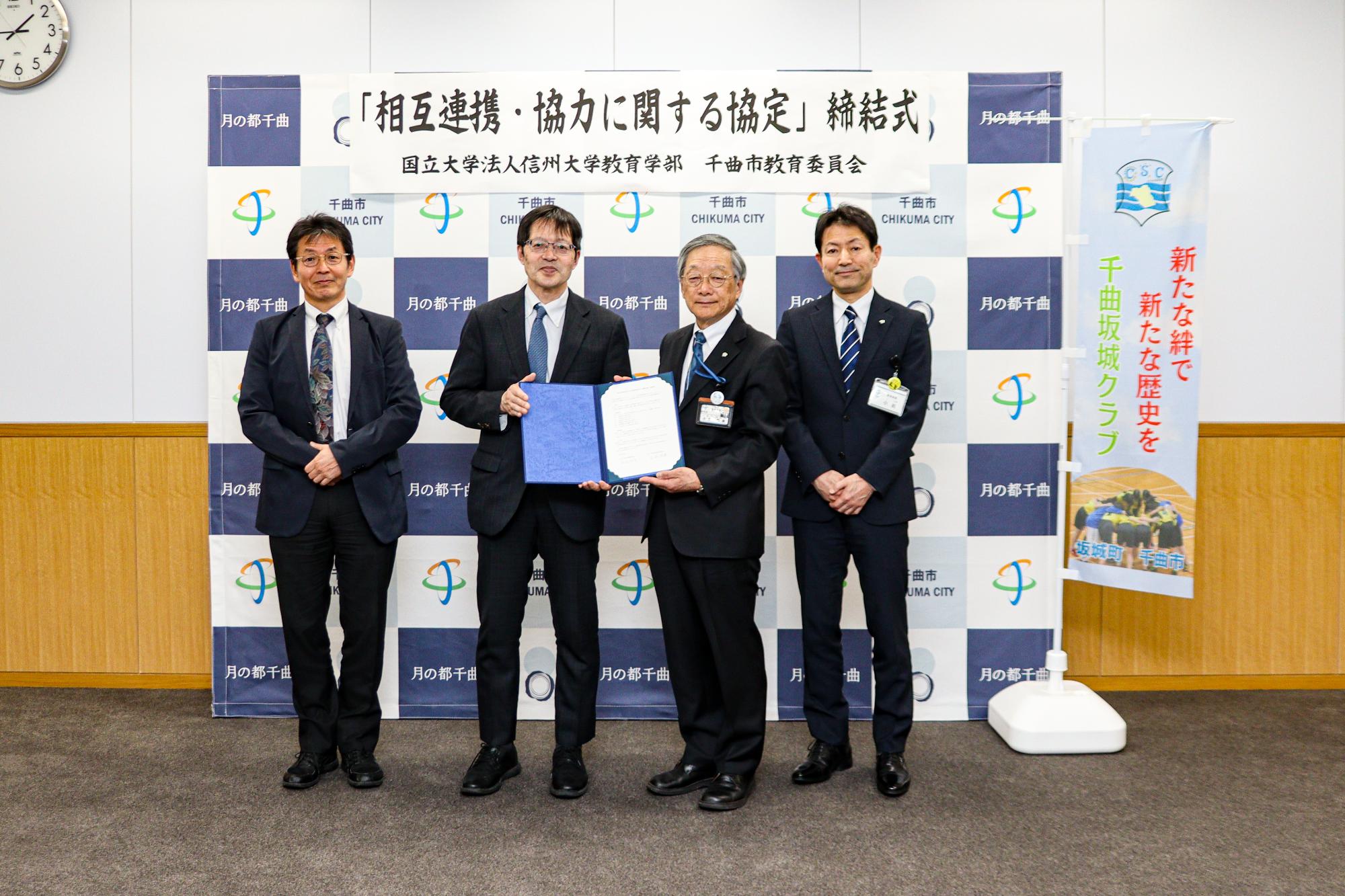 4人の男性が協定書を持って記念撮影している様子