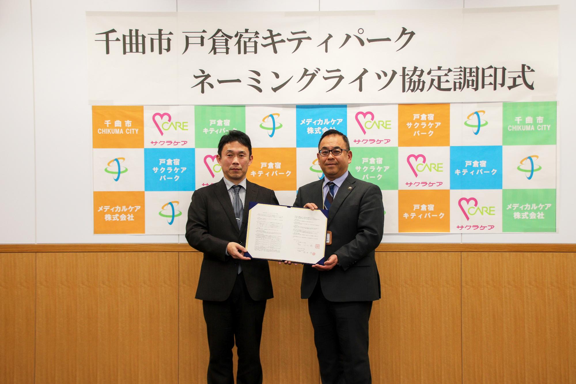 協定書を掲げるメディカルケア株式会社武田洋代表取締役社長と小川修一千曲市長