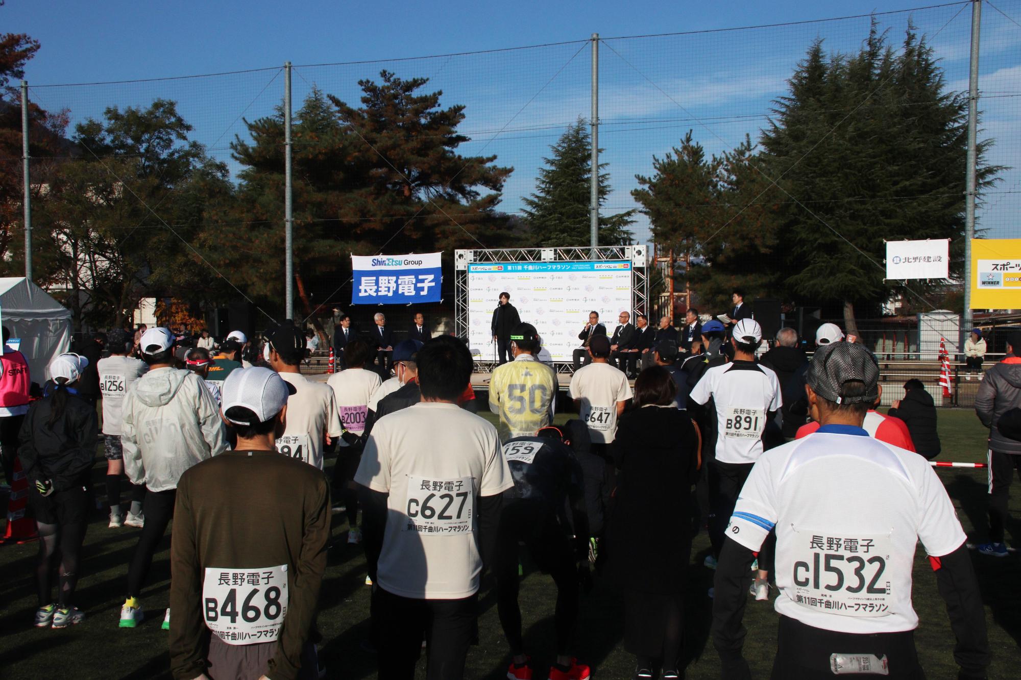 千曲市サッカー場での開会式で大会ゲスト小平奈緒さんの話を聞くランナーたち