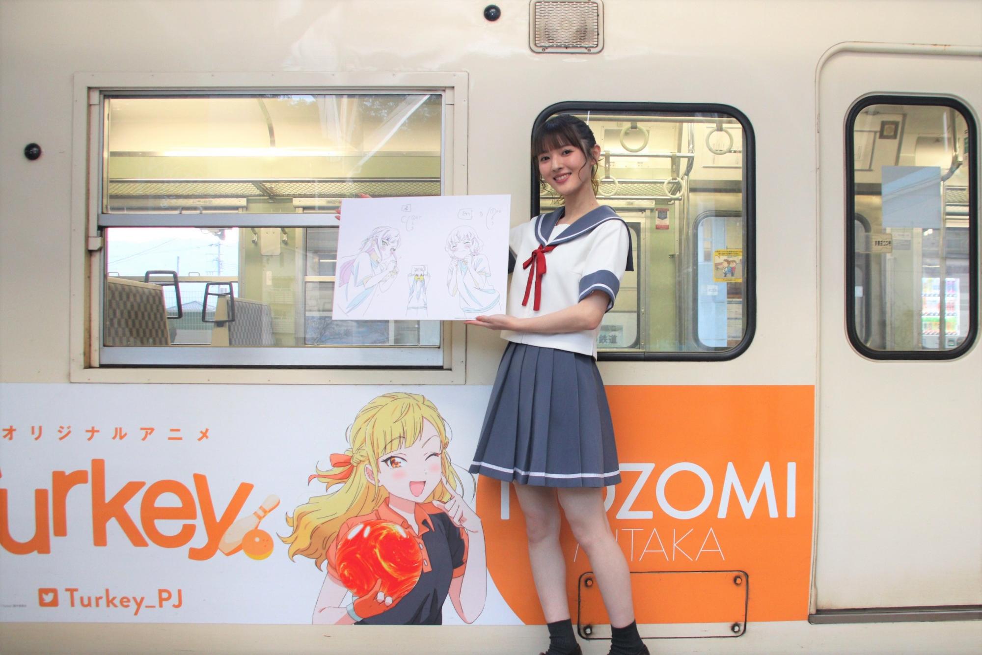 原画を持って車両ラッピングの前に立っている天麻ゆうきさん