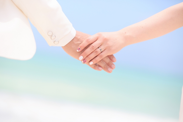 明るい海辺を背景に、新郎と新婦が手を重ねている写真