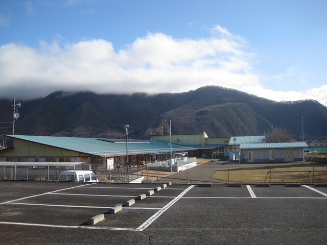 青い屋根の園舎と砂地と円形の芝の園庭の写真