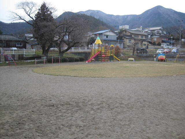 広い砂地に丸く芝生が生え、周りに遊具が設置された写真