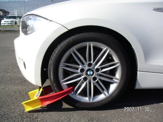 車の前方のタイヤに、黄色と赤色をした輪のような形をした部品が装着されている写真
