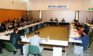 広々とした会議室でテーブルを四角に並べて座り会議を行う役員らの写真