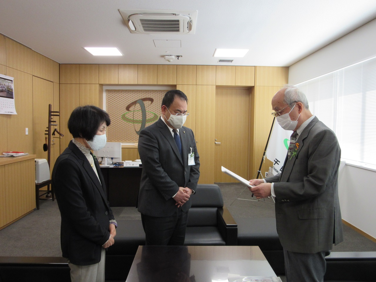 市長と会長、副会長がソファの近くで顔を向かい合わせるように立っている写真