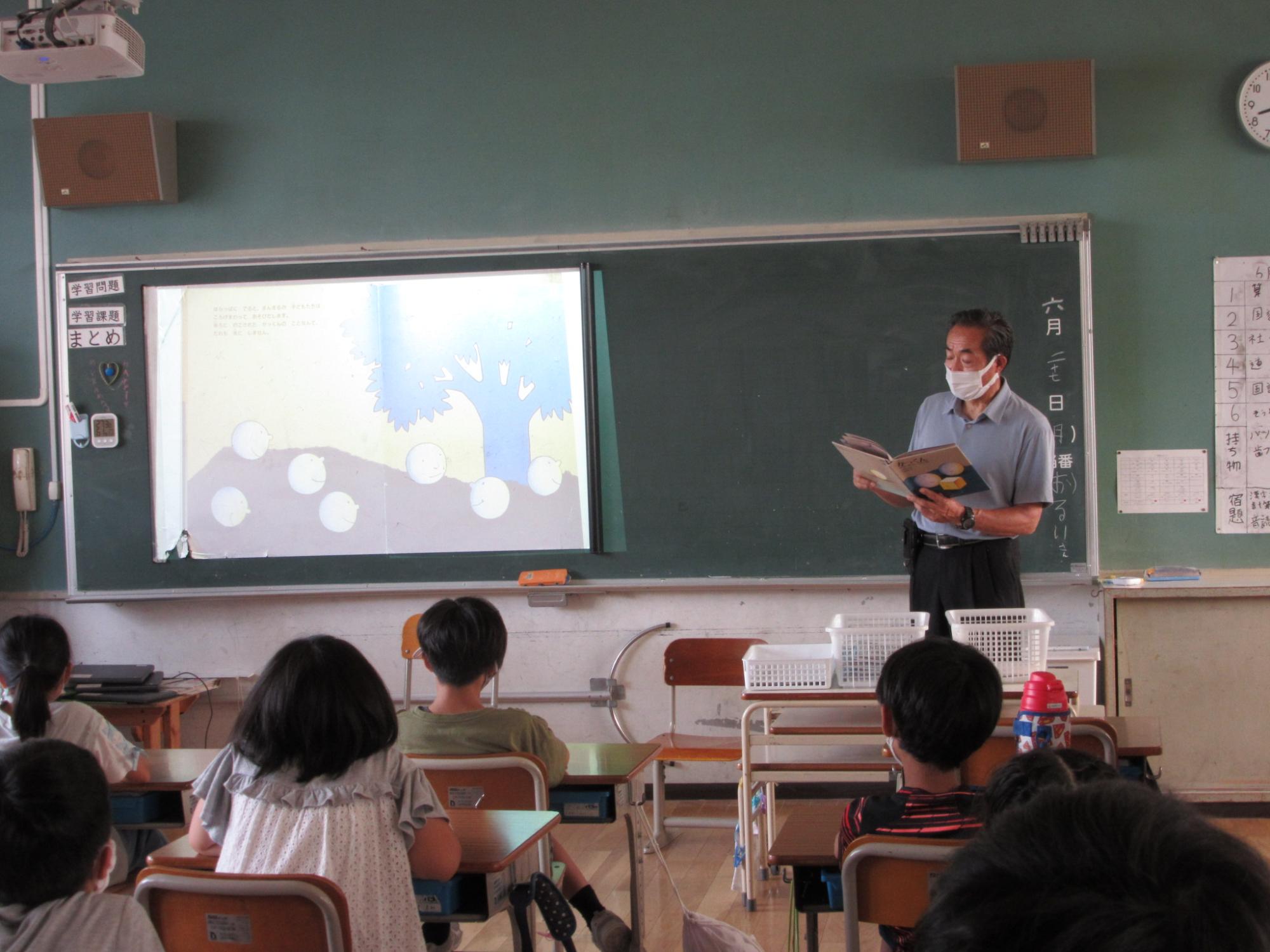 教室で机に座っている児童に読み聞かせを行っている様子