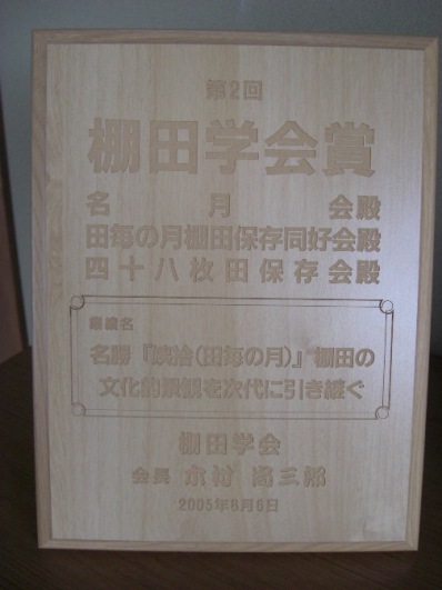 すべすべした木の板に、「第2回 棚田学会賞」といった文面が彫られている表彰状を撮影した写真