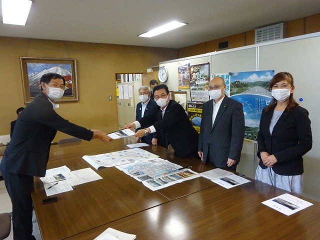 机を挟んで向かい合い、冊子を手渡している市長と建設部長の写真