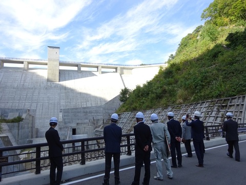関係者一同がヘルメット着用し、ダムを視察している写真