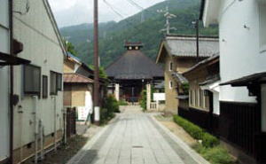 まっすぐな参道の奥に、三角形の屋根があるお寺の建物が建っている写真