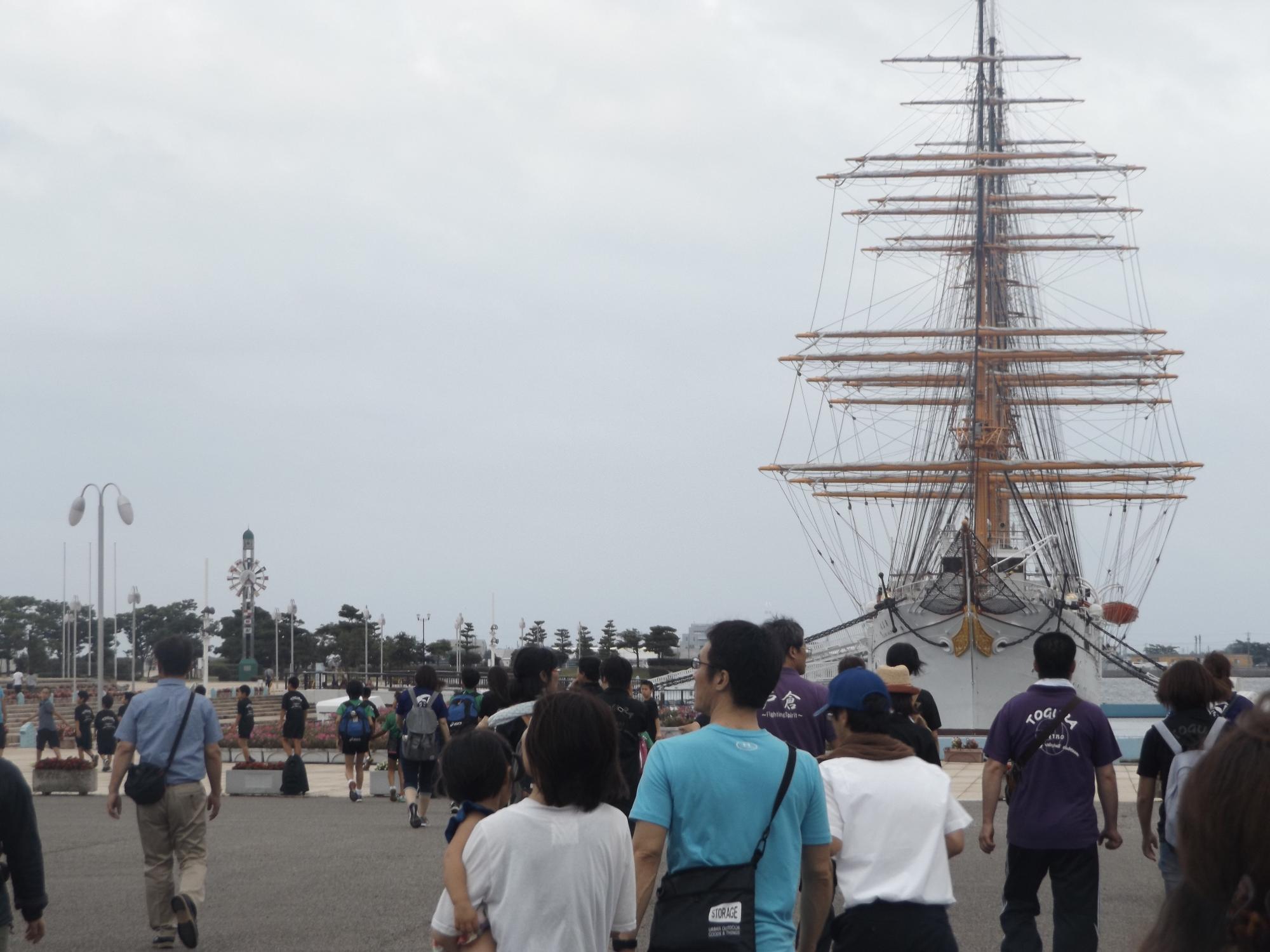 大きなマストが立っている船と、その周囲を歩いている観光客たちの写真