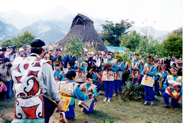 カラフルな衣装に身を包んだ人たちが縄文村で儀式を行っている写真