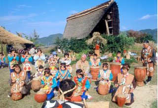 縄文村の広場で子供が並んで縄文太鼓の演奏を披露している写真